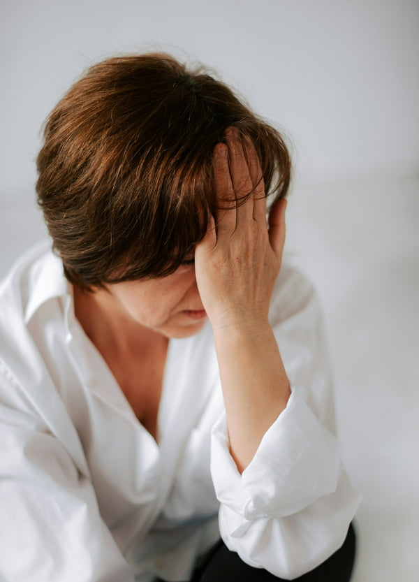 middle aged woman sitting on bed holding head in hands exhausted perimenopause symptoms fatigue